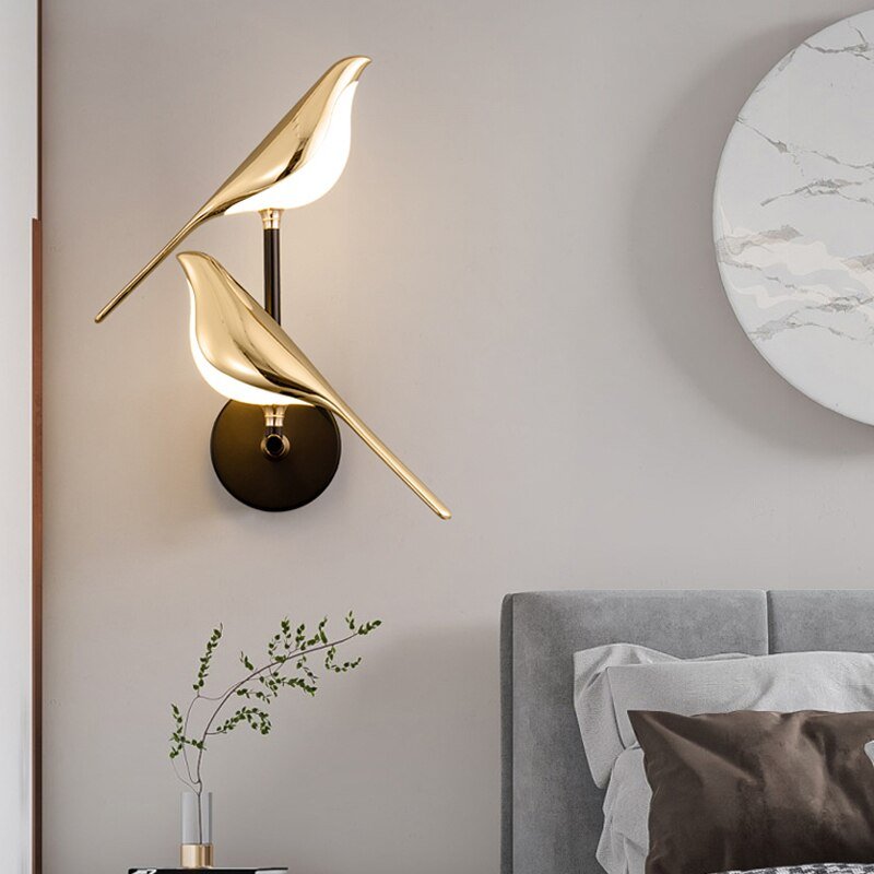 Auroria wandlamp met een elegant dubbel vogelontwerp in goud, stijlvol gemonteerd op een zwarte wandbeugel, creëert een artistieke en sfeervolle uitstraling in een moderne slaapkameromgeving.