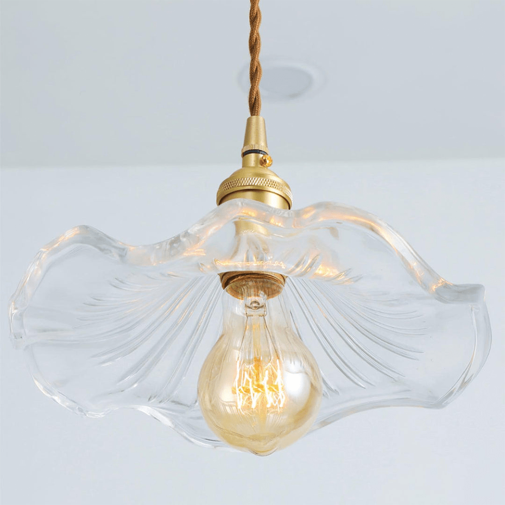 Close-up van de BloomLume hanglamp met een transparante, golvende glazen kap en een vintage gouden fitting. Deze stijlvolle en natuurlijke lamp biedt een warme gloed dankzij het decoratieve filamentlampje, ideaal voor een elegante en verfijnde sfeer in elk interieur.
