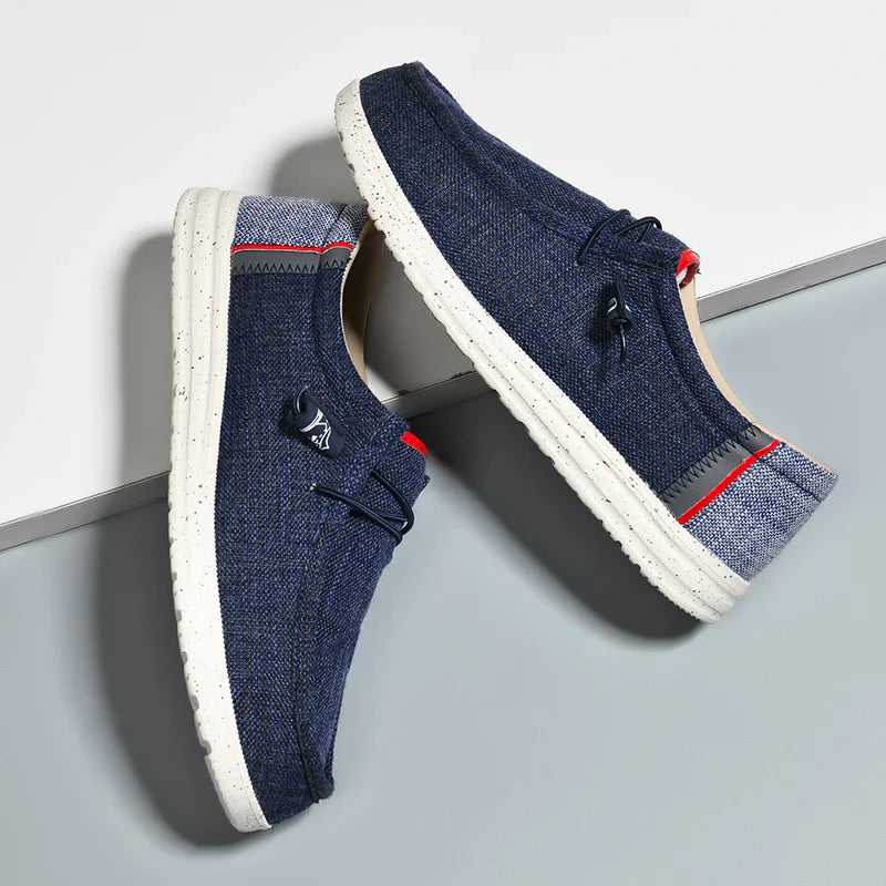 Blauwe canvas slip-on schoenen voor heren, ontworpen met ademende stof en een comfortabele, flexibele zool. Deze casual schoenen hebben sportieve rode en grijze details, waardoor ze zowel stijlvol als functioneel zijn voor dagelijks gebruik en wandelingen.