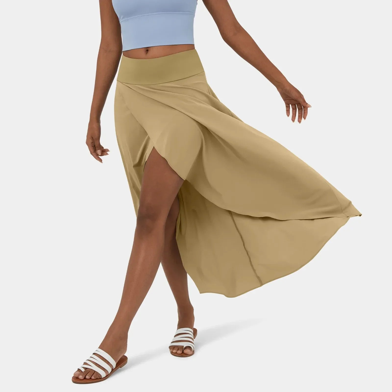 Een vrouw draagt een stijlvolle beige rok die elegant meebeweegt met haar bewegingen. De rok heeft een vloeiende snit die de benen mooi benadrukt en is gecombineerd met een lichtblauw sporttopje en witte sandalen, perfect voor een casual, doch verfijnde look.