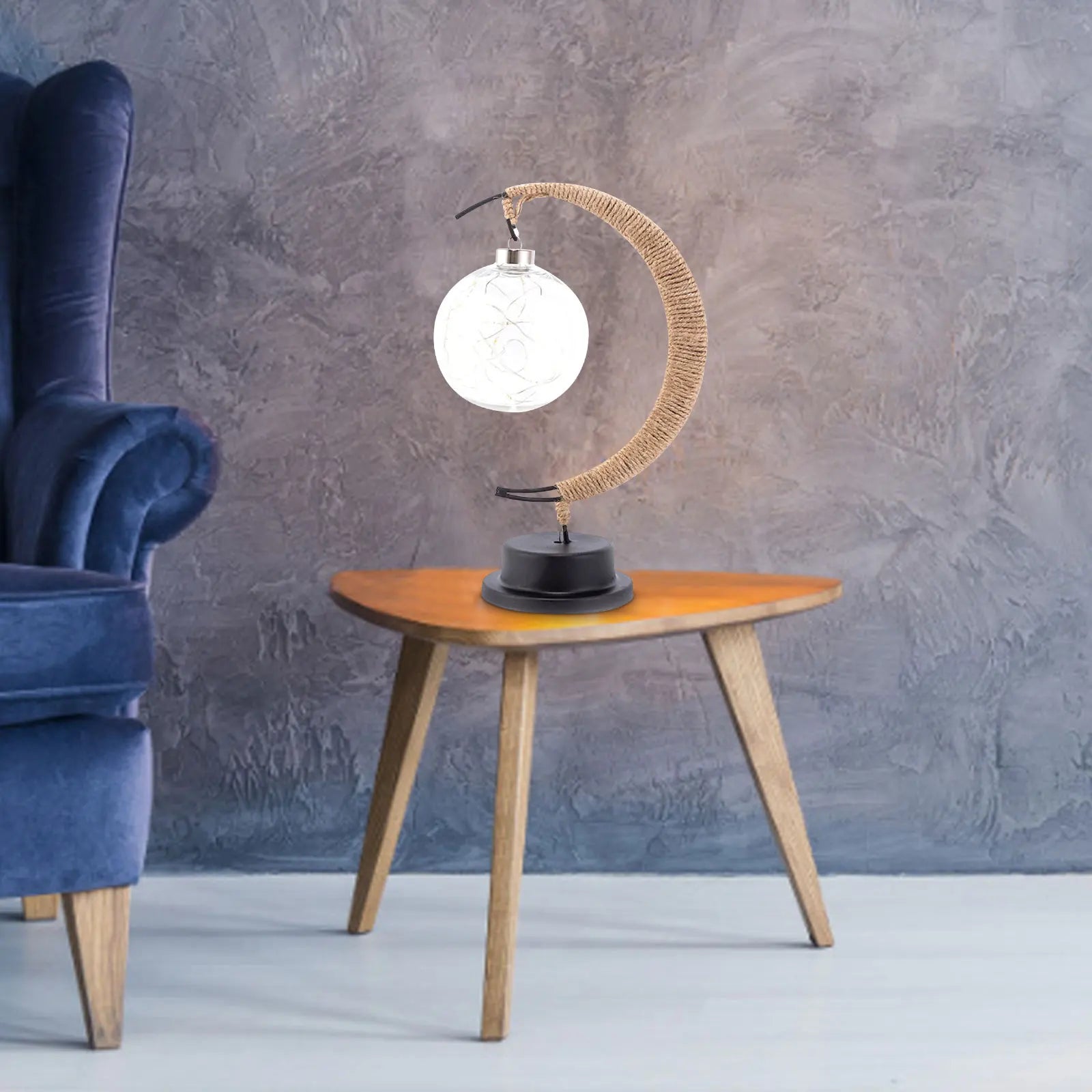 De GEMYNORA maanlamp, met een elegant design van een halfmaan en een verlichte bol, staat op een houten tafeltje naast een luxe blauwe stoel. Het zachte, magische licht van de lamp creëert een rustgevende en sfeervolle ambiance, perfect voor het verfraaien van elke kamer.