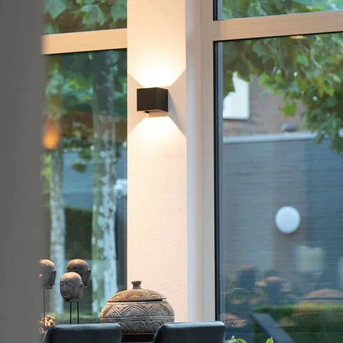 Een stijlvolle en moderne LED-wandlamp in een strak zwart vierkant ontwerp, gemonteerd aan de muur naast grote ramen, die de ruimte verlicht met zacht, gericht licht. Het ontwerp versterkt de eigentijdse esthetiek van de kamer.