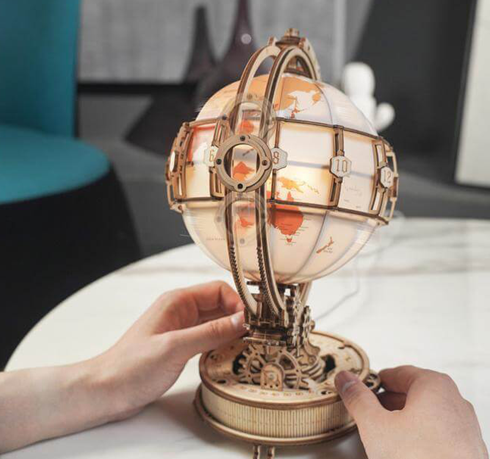Een persoon draait de Gloware Globus Luminous, een steampunk-geïnspireerde wereldbol met een verlichte kaart, die een warme en inspirerende sfeer creëert.