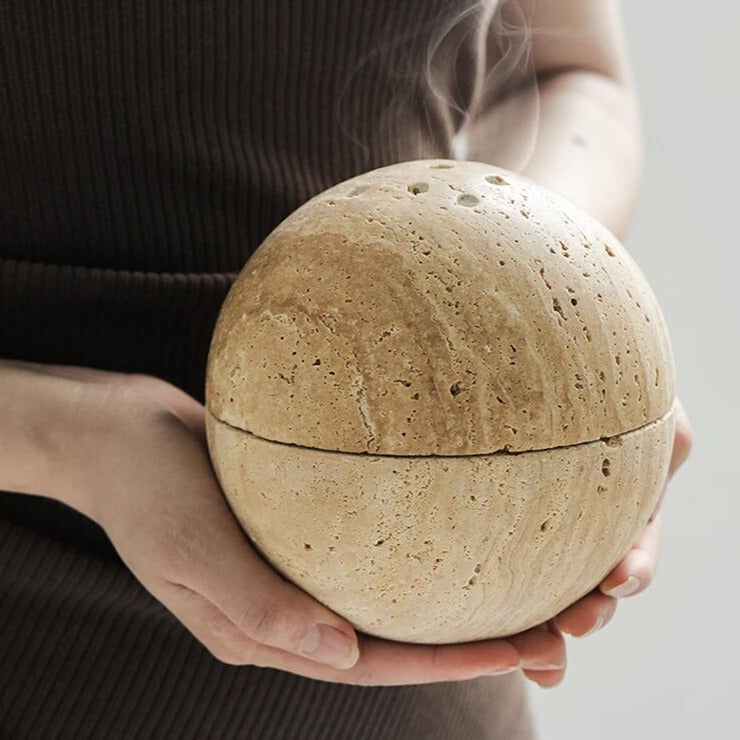 Grazia wierookhouder in een natuurlijke steenlook, vastgehouden door een persoon. De ronde vorm met subtiele openingen zorgt voor een rustgevend ontwerp, perfect voor meditatie en ontspanning in huis.
