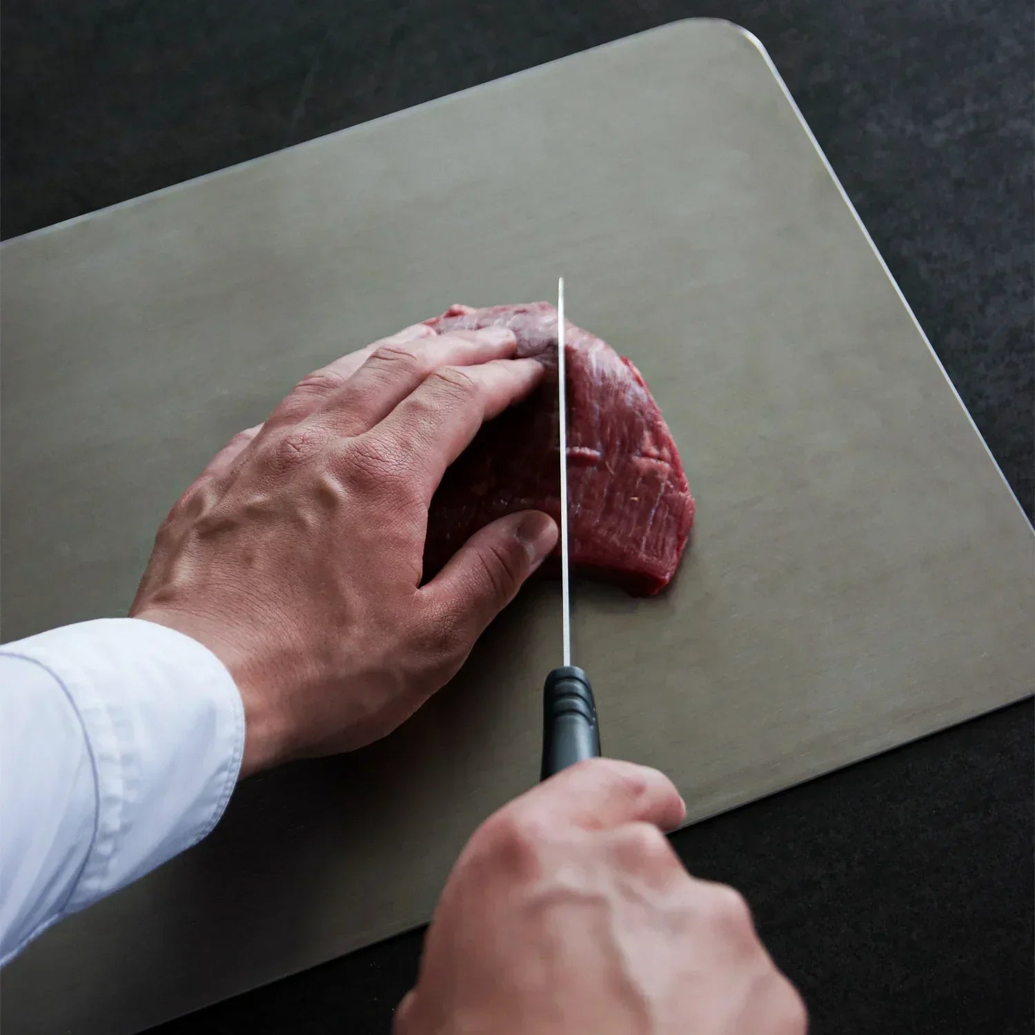Een duurzame Harmona snijplank van medisch titanium in gebruik, met een scherp mes dat moeiteloos door het vlees snijdt, ideaal voor langdurig gebruik in de keuken.