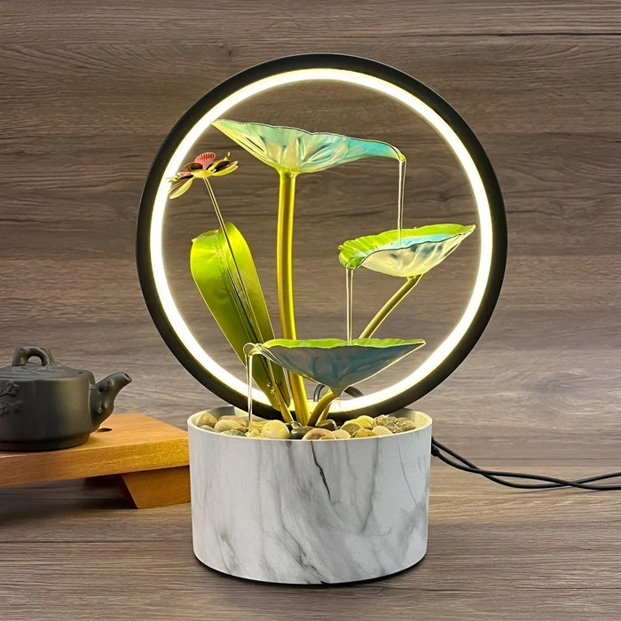 De Harmonia tafellamp, een elegante en veelzijdige verlichting met een marmeren basis, cirkelvormig LED-ontwerp en natuur geïnspireerde groene bladeren. De lamp biedt een harmonieus en rustgevend accent voor elk interieur.