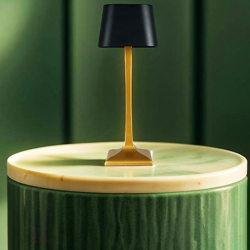 Helvona LED lamp met een strak en modern design, bestaande uit een goudkleurige standaard en een zwarte kap, geplaatst op een ronde, groene marmeren bijzettafel. Een stijlvolle en energiezuinige lamp die elegantie toevoegt aan elke ruimte en perfect is voor de woonkamer of slaapkamer.