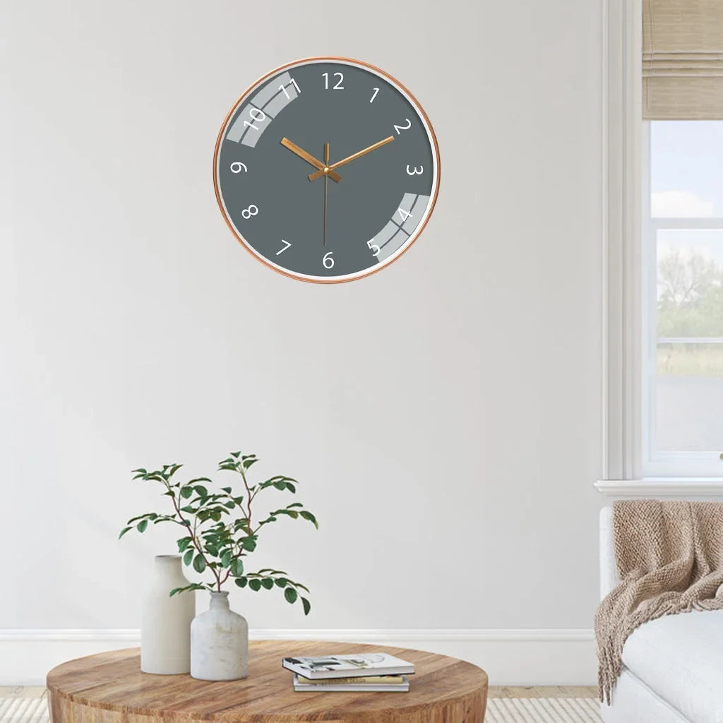 Jomera wandklok met stijlvol modern design, grijze wijzerplaat en gouden wijzers. De klok hangt in een minimalistisch ingerichte woonkamer boven een houten tafel met decoratieve accessoires. Perfect voor een eigentijdse en elegante uitstraling in huis.
