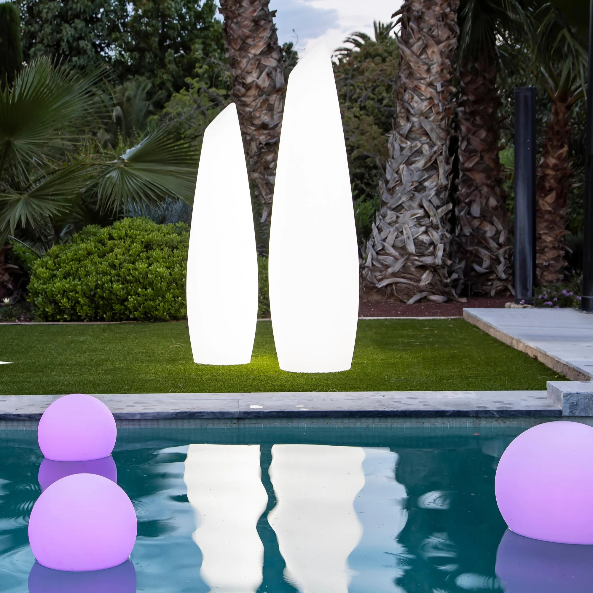 Sferische tuinverlichting van Kendra met grote, verlichte lampen in de vorm van kegelachtige objecten naast een zwembad, die de tuin sieren met een zachte gloed.