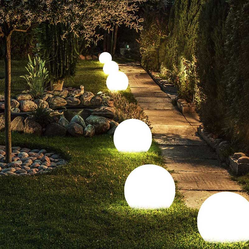 Sferische tuinverlichting van Kendra, met gloeiende witte bollen die een pad verlichten in een tuin, omgeven door groen en stenen.