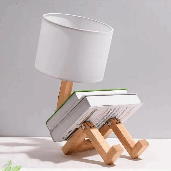 Klaarlicht tafellamp in een creatieve houding, zittend met een boek op schoot. De lamp heeft een houten verstelbaar frame en een eenvoudige witte lampenkap. Perfect als functionele decoratie in een modern interieur.