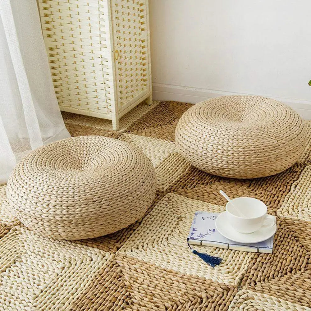 Luma kussens met een elegant, handgeweven ontwerp in een natuurlijke tint, geplaatst op een geweven tapijt. De kussens hebben een ronde en comfortabele vorm, perfect voor zitplekken of decoratie. Ze voegen een warme en rustieke sfeer toe aan je interieur.