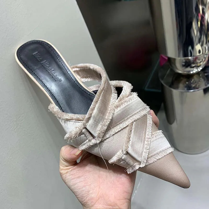 Een close-up van een beige Lumenza sandaal met gekruiste banden, een puntige neus en een comfortabele hak, perfect voor een stijlvolle en gemakkelijke look.