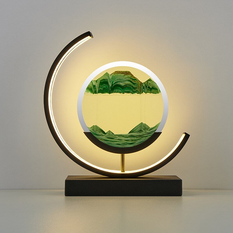 De LumiAura lamp toont een fascinerend zandlandschap in groene tinten, dat langzaam beweegt en de betoverende werking van het zand benadrukt. Het ontwerp, met een modern metalen frame en een zachte lichtcirkel, creëert een rustgevende sfeer in elke ruimte. Het is niet alleen een lamp, maar een kunstwerk dat elegantie en kalmte uitstraalt, perfect voor interieurdecoratie die zowel stijlvol als kalmerend is.