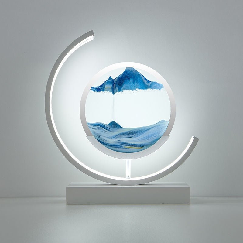 Deze betoverende lamp van LumiAura creëert een magische sfeer met zijn kalmerende blauwe zandlandschap, dat zachtjes verandert. Het elegante ontwerp met een cirkelvormig frame en subtiele verlichting voegt een artistiek element toe aan elke ruimte, perfect voor het creëren van een serene en ontspannen omgeving. Het zachte licht en het verstrijkende zand zorgen voor een unieke ervaring die je kamer verlicht en verrijkt.