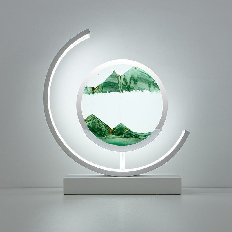 Deze betoverende lamp van LumiAura toont een prachtig zandlandschap in groene tinten, met het zand dat langzaam beweegt in het verlichte frame. Het moderne, minimalistische ontwerp creëert een rustgevende sfeer en voegt een vleugje kunst toe aan je interieur. Het zachte, omhullende licht zorgt voor een warme en uitnodigende omgeving, perfect voor ontspanning en meditatie.