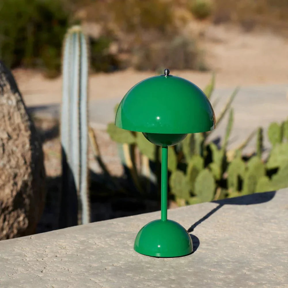Een moderne groene LumiNova tafellamp met een opvallende bolvormige kap en een slanke voet, geplaatst in een buitenomgeving naast cactussen. Deze stijlvolle LED-lamp biedt functionele en sfeervolle verlichting, ideaal voor zowel binnen- als buitenruimtes.