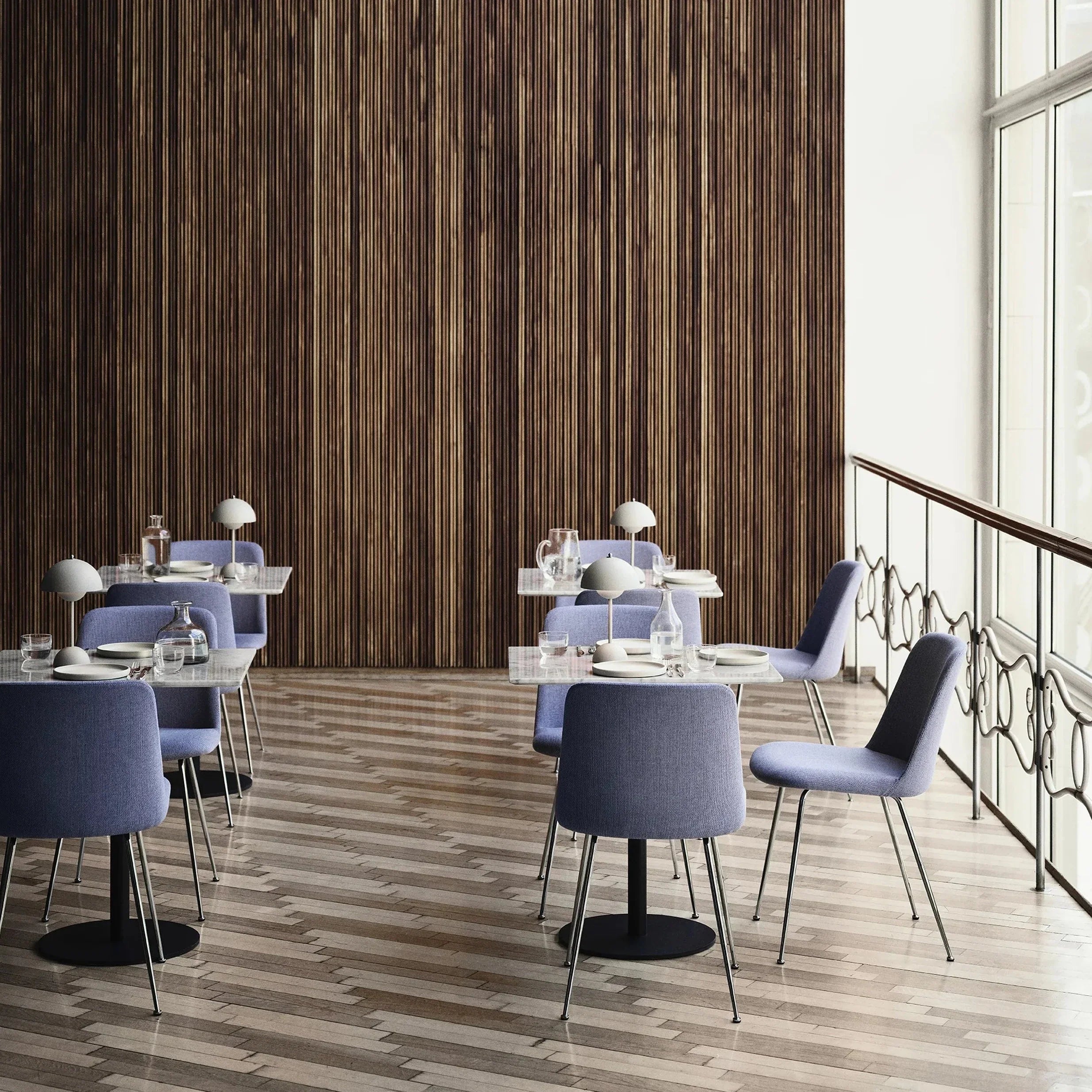 Een moderne eetruimte met vier stijlvolle tafels, elk verlicht door een LumiNova tafellamp LED. De lampen, met hun elegante bolvormige kappen, zorgen voor sfeervolle verlichting in de ruimte, omringd door minimalistische stoelen en een warme houten wand. Perfect voor een verfijnde en gezellige eetervaring.