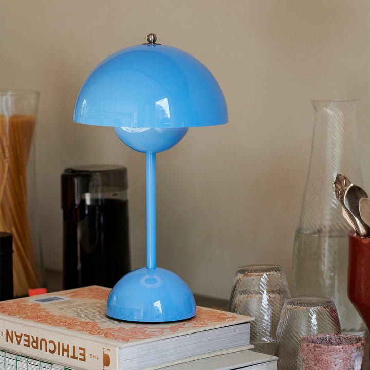Een LumiNova tafellamp LED in het blauw staat stijlvol bovenop een stapel boeken op een houten tafel. De lamp heeft een modern ontwerp met een ronde basis en een halfronde kap die het licht verspreidt, wat bijdraagt aan een eigentijdse en verfijnde uitstraling. De lamp is perfect voor het verfraaien van een bureau of nachtkastje.