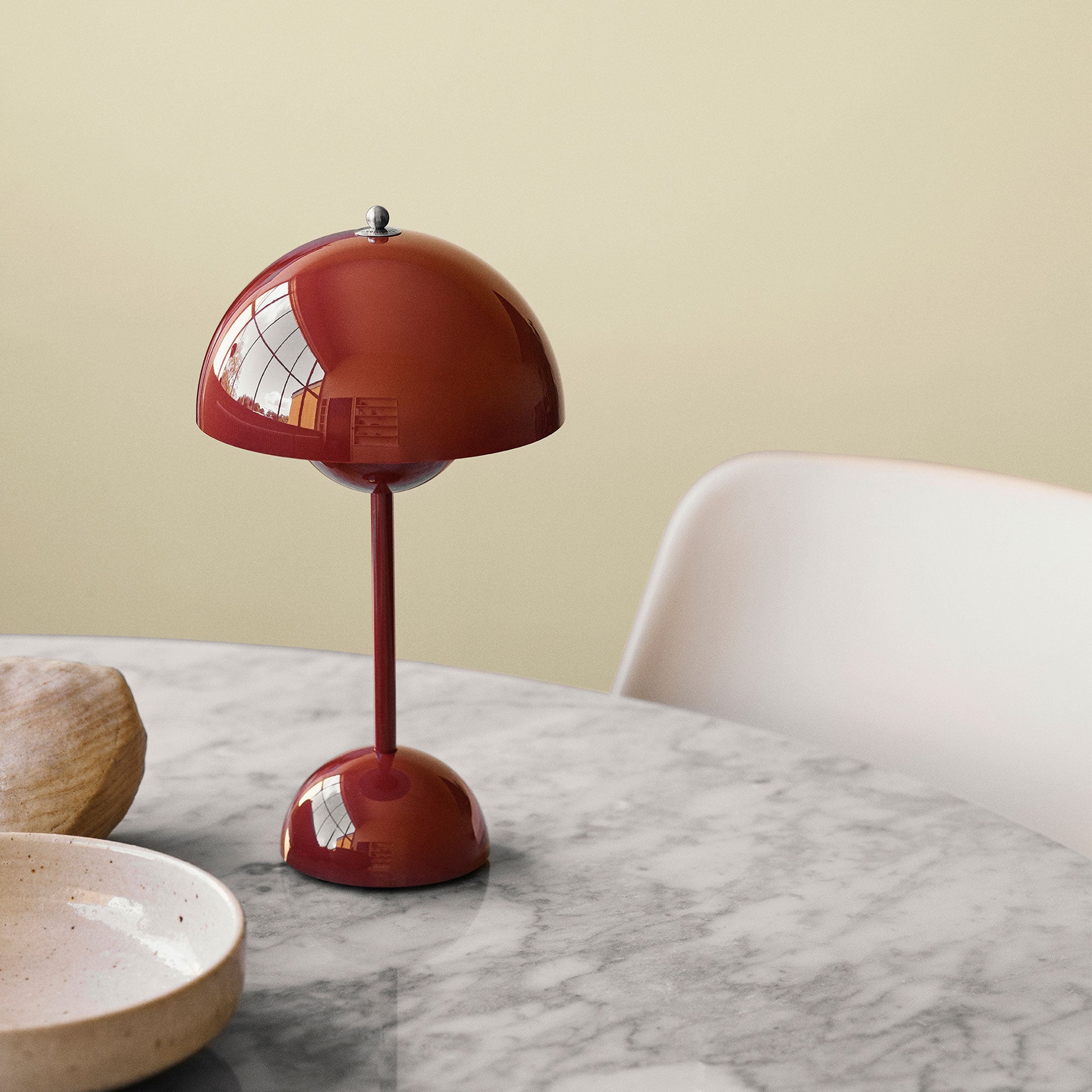 Een elegante LumiNova tafellamp in een warme bordeauxrode kleur, geplaatst op een marmeren tafel. De lamp heeft een minimalistische uitstraling met een halfronde kap en een slanke, ronde basis, ideaal voor het creëren van stijlvolle verlichting in moderne interieurs.