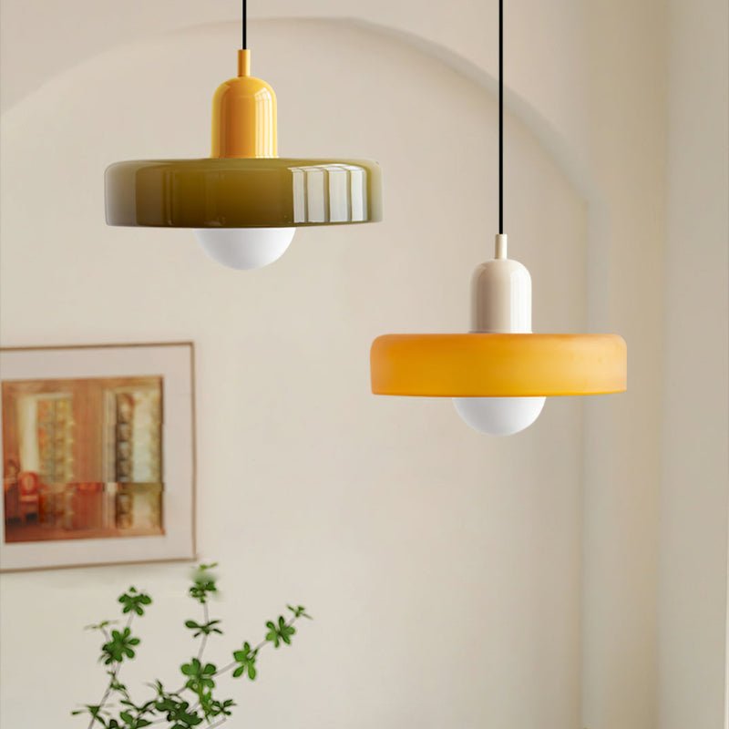 Twee Luminezza Living hanglampen in een kleurrijk design, harmonieus gecombineerd in een minimalistische kamer. De geelgroene en warme oranje tinten van de lampenkappen voegen een speelse en moderne uitstraling toe, ideaal voor het verlichten van woon- of eetruimtes met een stijlvol accent.