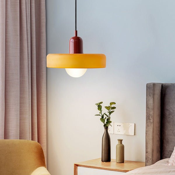 De Luminezza Living hanglamp in kleurrijk design is afgebeeld in een moderne slaapkameropstelling, met een warme gele kap en bordeauxrode details. Deze stijlvolle lamp biedt een sfeervolle verlichting en voegt een speels accent toe aan het interieur.