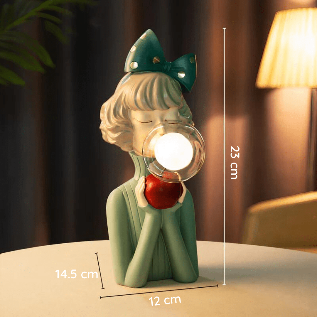 Luminique tafellamp met een elegant en modern ontwerp, afgebeeld als een vrouwelijke figuur met een groene strik en een rode appel. De lamp is 23 cm hoog en 14,5 cm breed, voorzien van een sfeervolle LED-lichtbron in een glazen bol. Een unieke decoratieve verlichting voor een stijlvolle en eigentijdse ruimte.