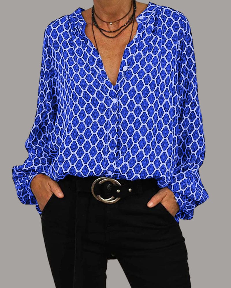 Blouse met een geometrisch patroon in blauw en wit, gedragen door een vrouw met een zwarte broek en een opvallende leren riem, geschikt voor een elegante en modieuze look.