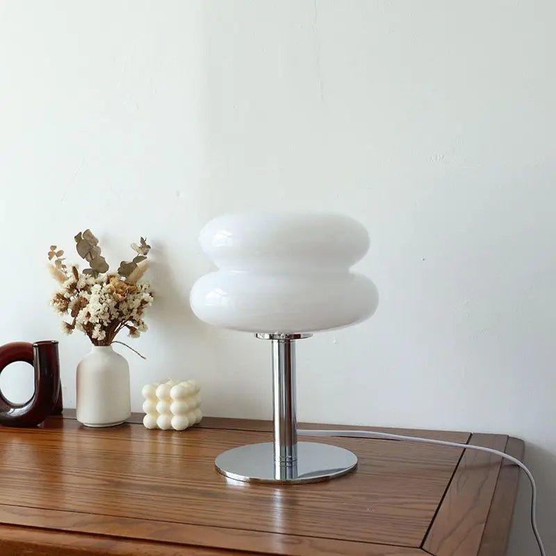 Iconische Luminore Design tafellamp in een elegante witte uitvoering, met een dubbele glazen kap en een glanzende metalen voet. Geplaatst op een houten tafel met subtiele decoratieve elementen, ideaal om een tijdloze en verfijnde sfeer aan uw interieur toe te voegen.