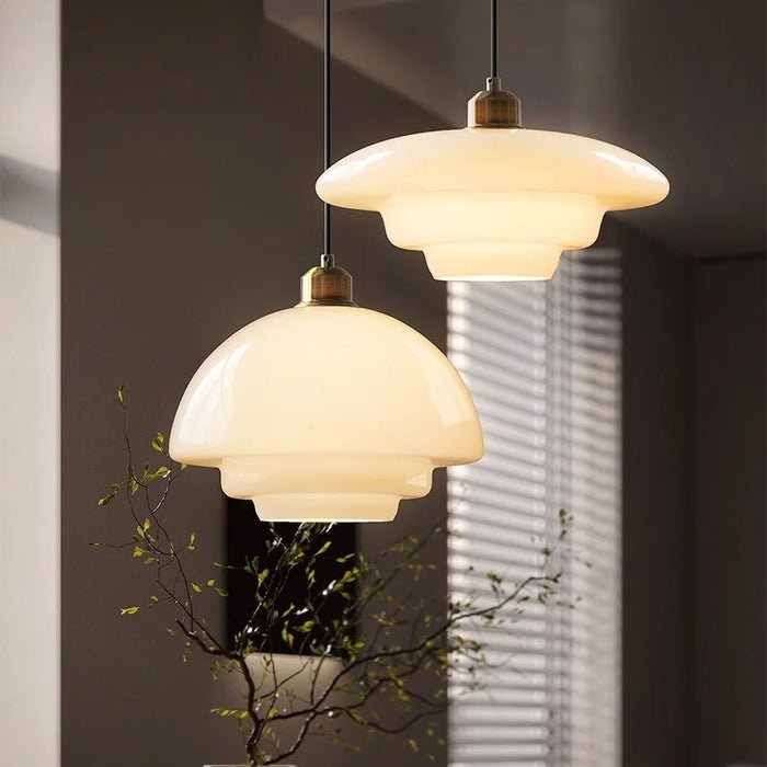 Twee elegante witte glazen hanglampen hangen boven een tafel, stralend met een zachte, warme gloed. Het moderne ontwerp heeft gelaagde glazen lampenkappen en een minimalistische afwerking, die perfect in een stijlvolle ruimte passen. Het subtiele ontwerp biedt zowel verlichting als een verfijnd decoratief element.