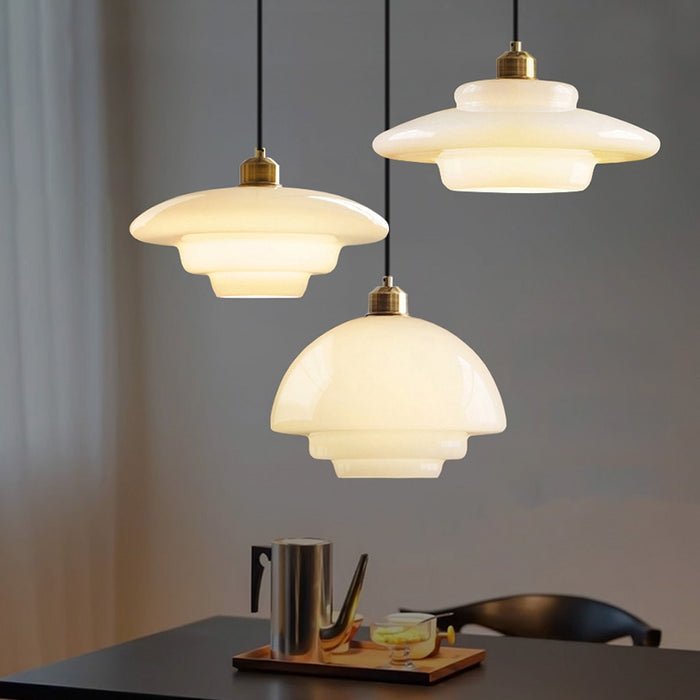 Elegante witte glazen hanglampen met een subtiel gelaagd ontwerp, perfect voor moderne interieurs. De lampen hangen in een set van drie, elk met een zachte, diffuse lichtuitstraling, wat zorgt voor een warme en sfeervolle ambiance. De gouden details voegen een vleugje verfijning toe aan het design.