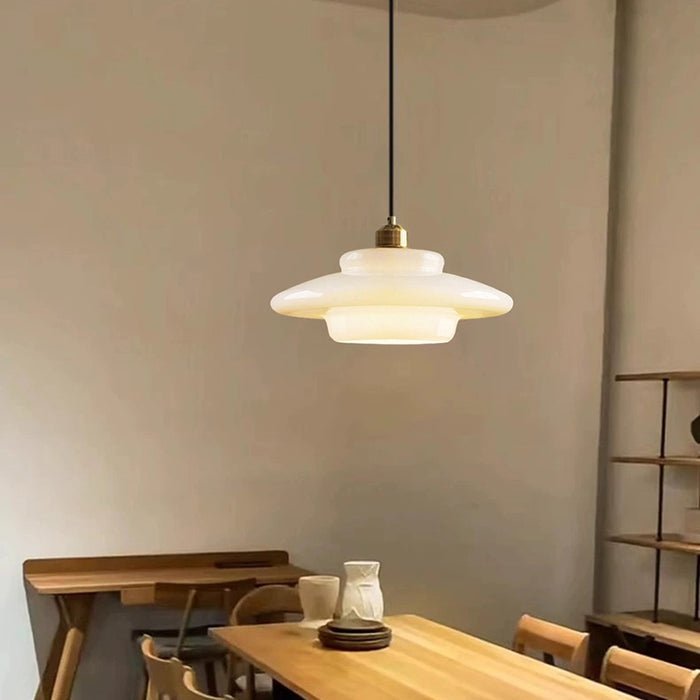 Elegante witte glazen hanglamp met een gelaagd ontwerp, afgewerkt met gouden details. De lamp creëert een warme en verfijnde sfeer, perfect voor moderne eetkamers of andere stijlvolle interieurinstellingen. Het subtiele, diffuse licht maakt het een ideale keuze voor sfeerverlichting.