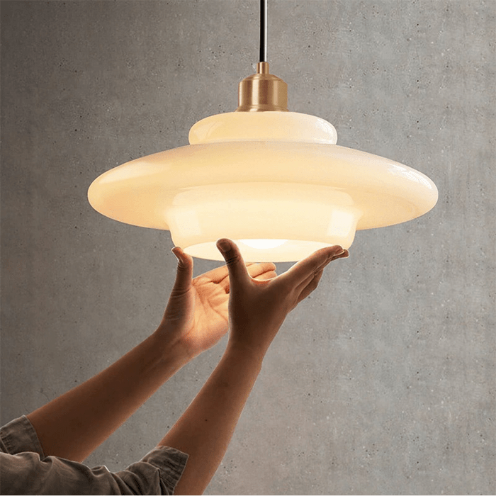 Een elegante witte glazen hanglamp in een modern ontwerp, voorzichtig vastgehouden terwijl deze wordt geïnstalleerd. De lamp heeft een verfijnd, gelaagd ontwerp met een warme, uitnodigende gloed, perfect voor het creëren van een stijlvol sfeerlicht in elke ruimte.
