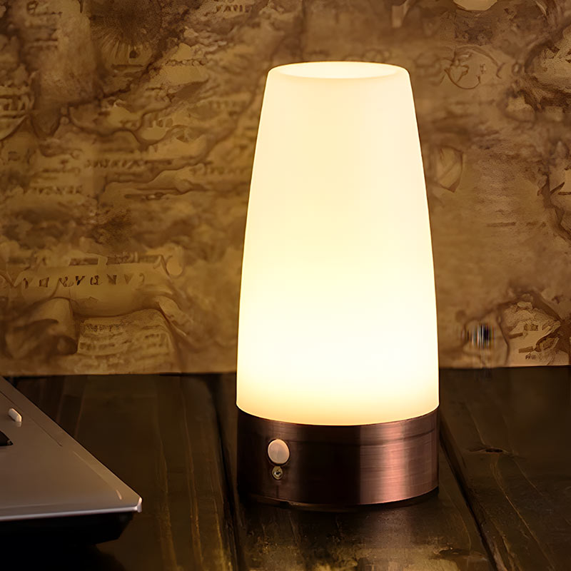 Luvora tafellamp met sfeervol warm licht, geplaatst op een houten tafel tegen een decoratieve achtergrond. De lamp heeft een moderne uitstraling met een metalen basis en een matglazen kap. Perfect voor het creëren van een gezellige sfeer in huis, ideaal voor nachtkastjes of bureaus.