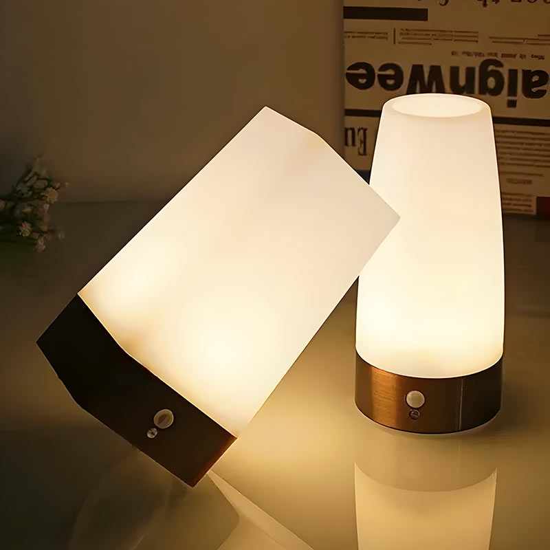 Twee Luvora tafellampen met sfeervol licht, één rechtop en de ander schuin geplaatst op een tafel. De lampen hebben een modern design met een houten basis en een matglazen kap die een warme, gezellige gloed verspreidt. Perfect voor een rustgevende sfeer in de woonkamer of slaapkamer.