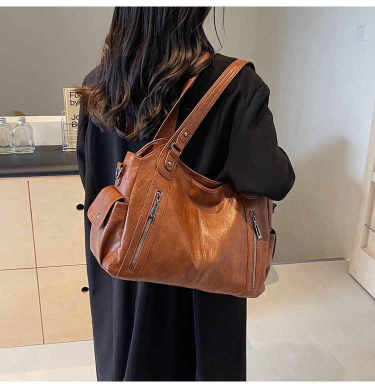 OLYNDA bruine leren tote tas gedragen over de schouder met een moderne en praktische uitstraling, perfect voor dagelijks gebruik.