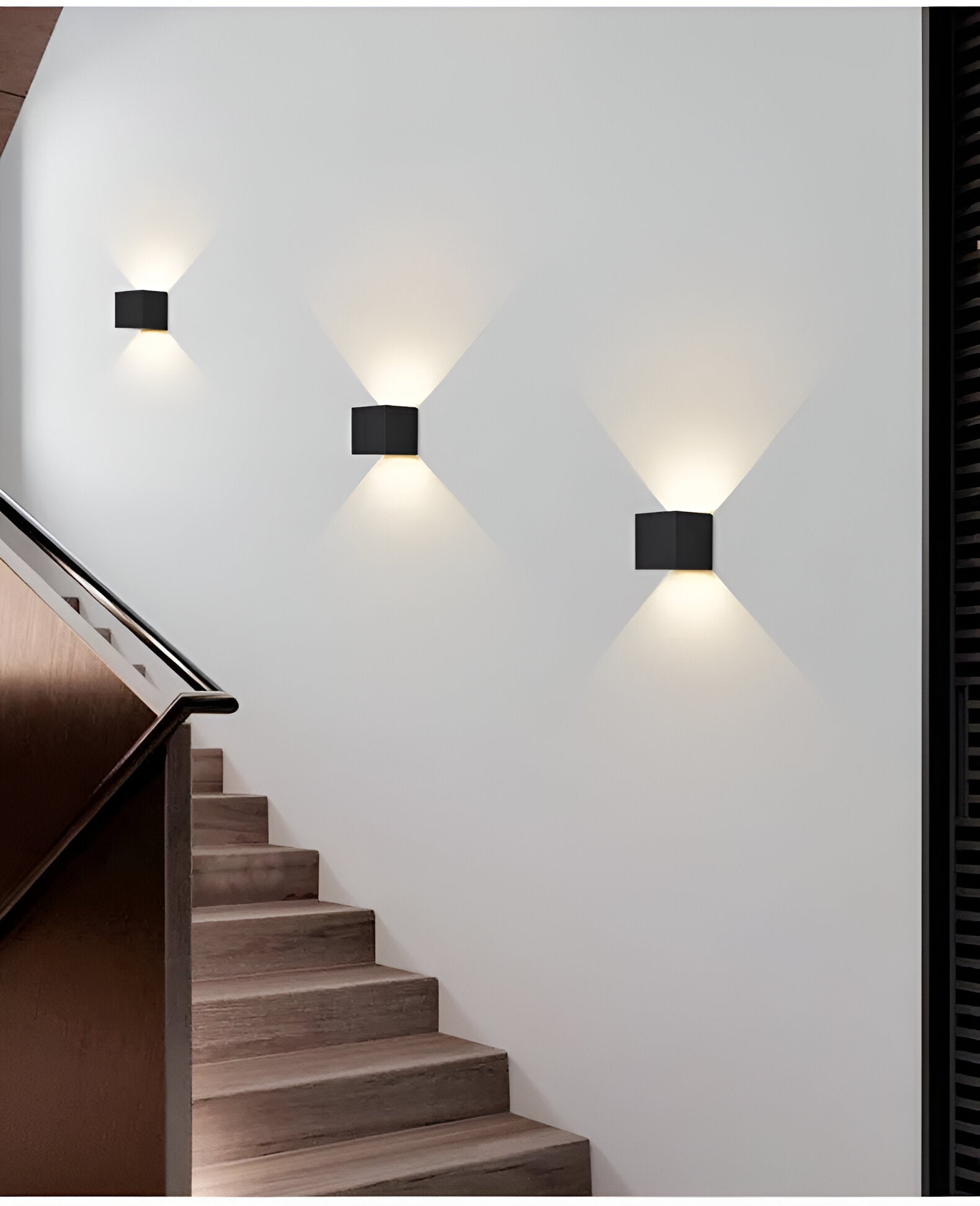 Omnira Glow verstelbare wandlampen in zwart gemonteerd op een muur naast een houten trap, met een zachte, diagonale lichtuitstraling die de trap verlicht.