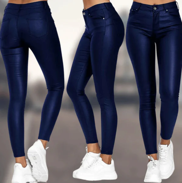 Een vrouw draagt een elegante, donkerblauwe, hoog-taille broek van Onyx met een strakke pasvorm. De broek heeft een subtiele glans en is gecombineerd met een paar witte sneakers voor een moderne, casual look.