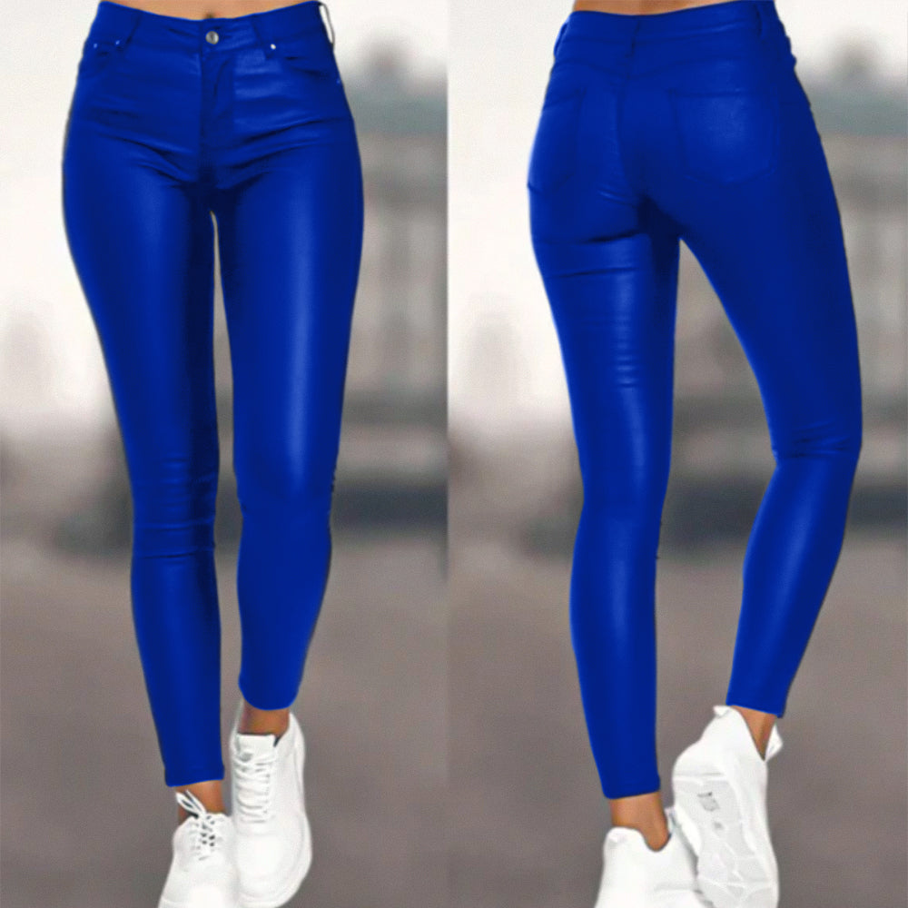 Een vrouw draagt een strakke, blauwe hoog-taille broek van Onyx met een leren uitstraling. De broek is perfect gestyled met witte sneakers voor een moderne en chique uitstraling.