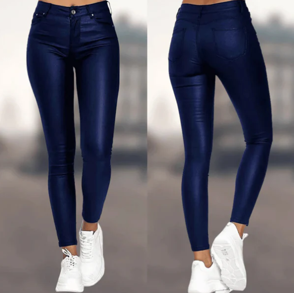 Een vrouw draagt een elegante, donkerblauwe, hoog-taille broek van Onyx, met een strakke pasvorm en een moderne uitstraling. De broek is afgewerkt met een subtiele glans en is gecombineerd met een paar witte sneakers.