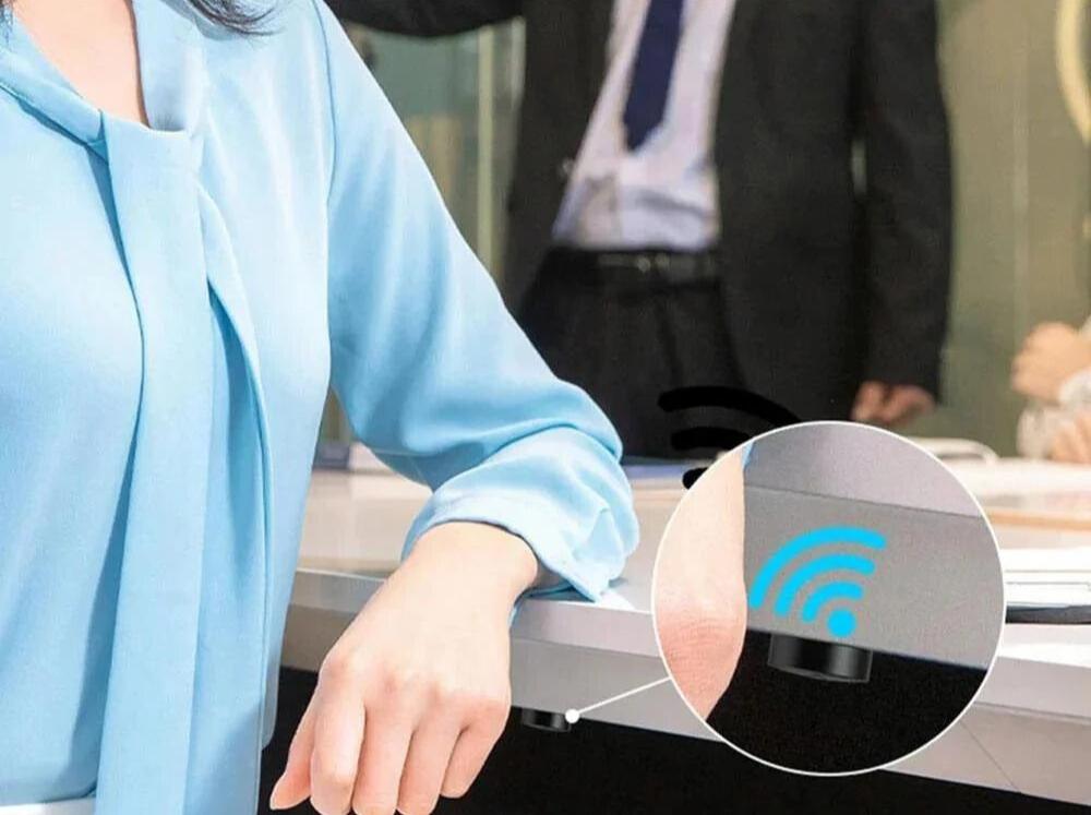 Orbitron GPS Tracker met krachtige magnetische bevestiging, bevestigd onder een bureau. De afbeelding toont de tracker verborgen onder het tafelblad, met een close-up van de tracker die draadloze connectiviteit aangeeft.