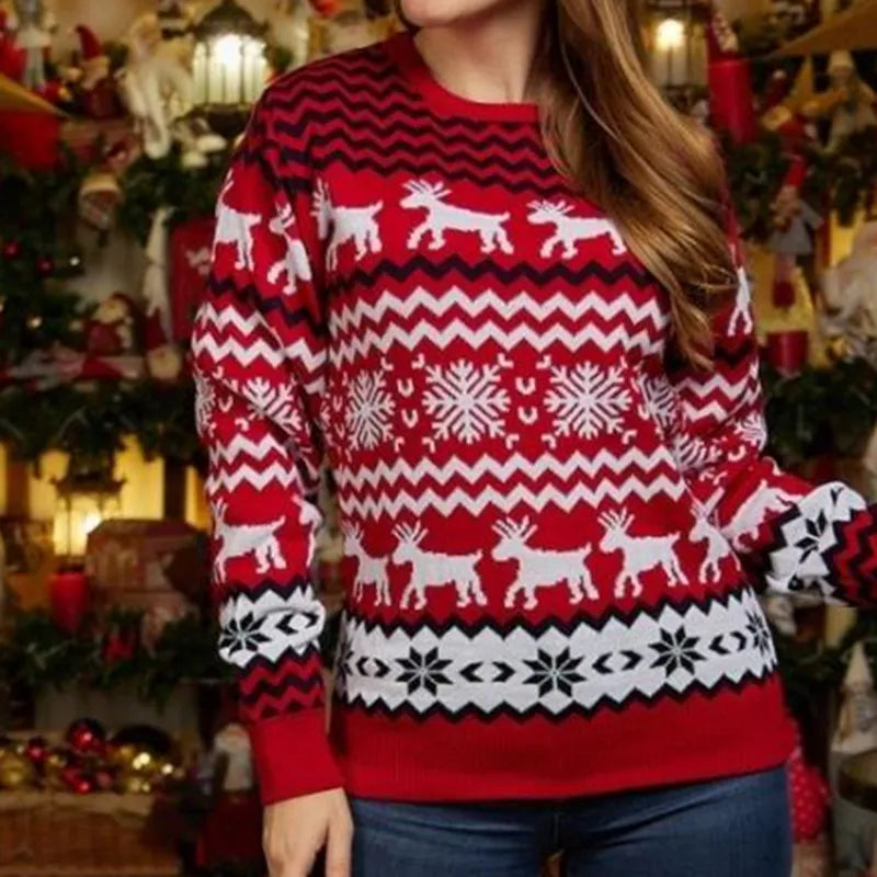 Een vrouw draagt een rode kersttrui met een festieve print van rendieren, sneeuwvlokken en zigzagpatronen in wit en zwart. De trui is stijlvol en comfortabel, perfect voor de feestdagen.