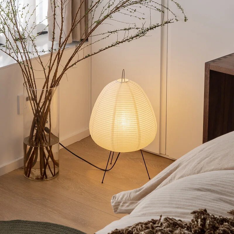 De Prana lamp met een stijlvolle papieren lampenkap en minimalistische metalen poten creëert een warme, verfijnde sfeer. Perfect voor een slaapkamer of woonkamer, straalt het zachte licht rust uit en past het moeiteloos in moderne interieurs.