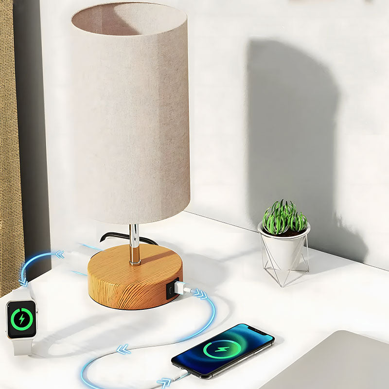 Solvani bedlamp met een eigentijds ontwerp, geplaatst op een bureau. De lamp heeft een houten voet met ingebouwde USB-poort, waarmee een smartwatch en smartphone tegelijkertijd worden opgeladen. De cilindervormige kap zorgt voor een zachte verlichting, perfect voor een moderne en sfeervolle werk- of slaapkamer.
