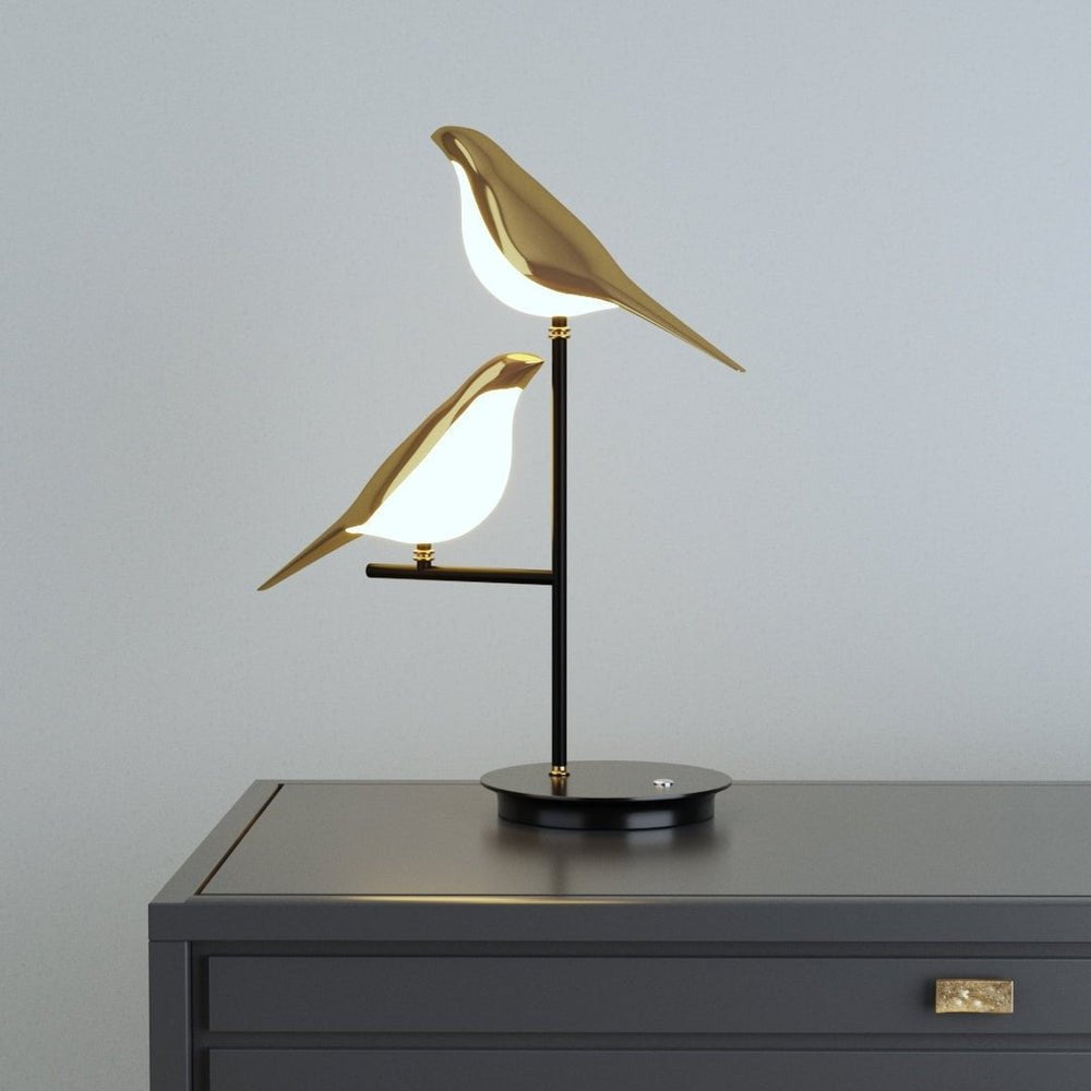 Elegante Sprankelum LED Tafellamp met een verfijnd design van twee goudkleurige vogels op een zwarte standaard. Perfect als sfeervolle verlichting voor moderne interieurs, ideaal voor op een dressoir of nachtkastje.
