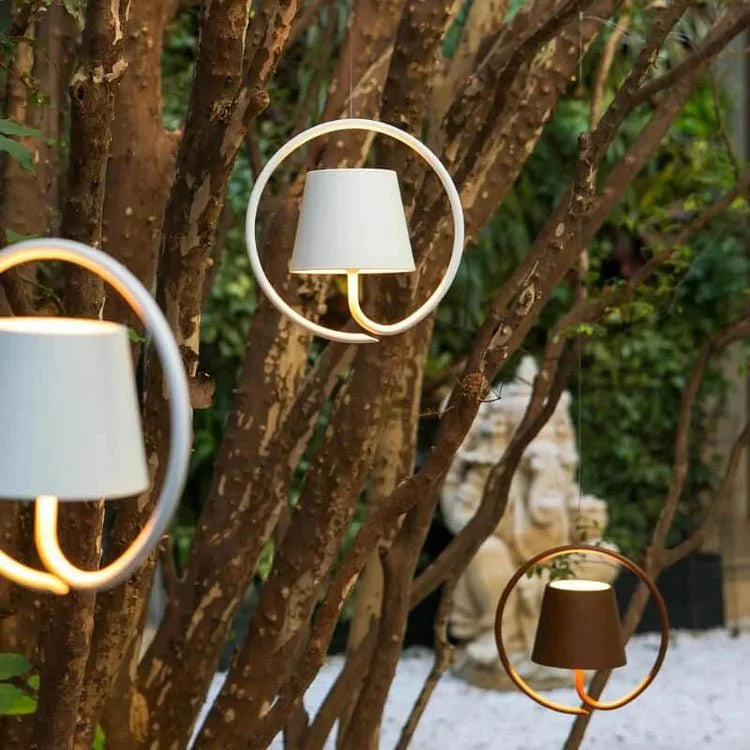 Stijlvolle Stralendthuis hanglampen in verschillende kleuren, subtiel opgehangen tussen bomen in een tuin, ontworpen met een elegant cirkelvormig frame en duurzame, weerbestendige materialen, perfect voor sfeervolle buitenverlichting.