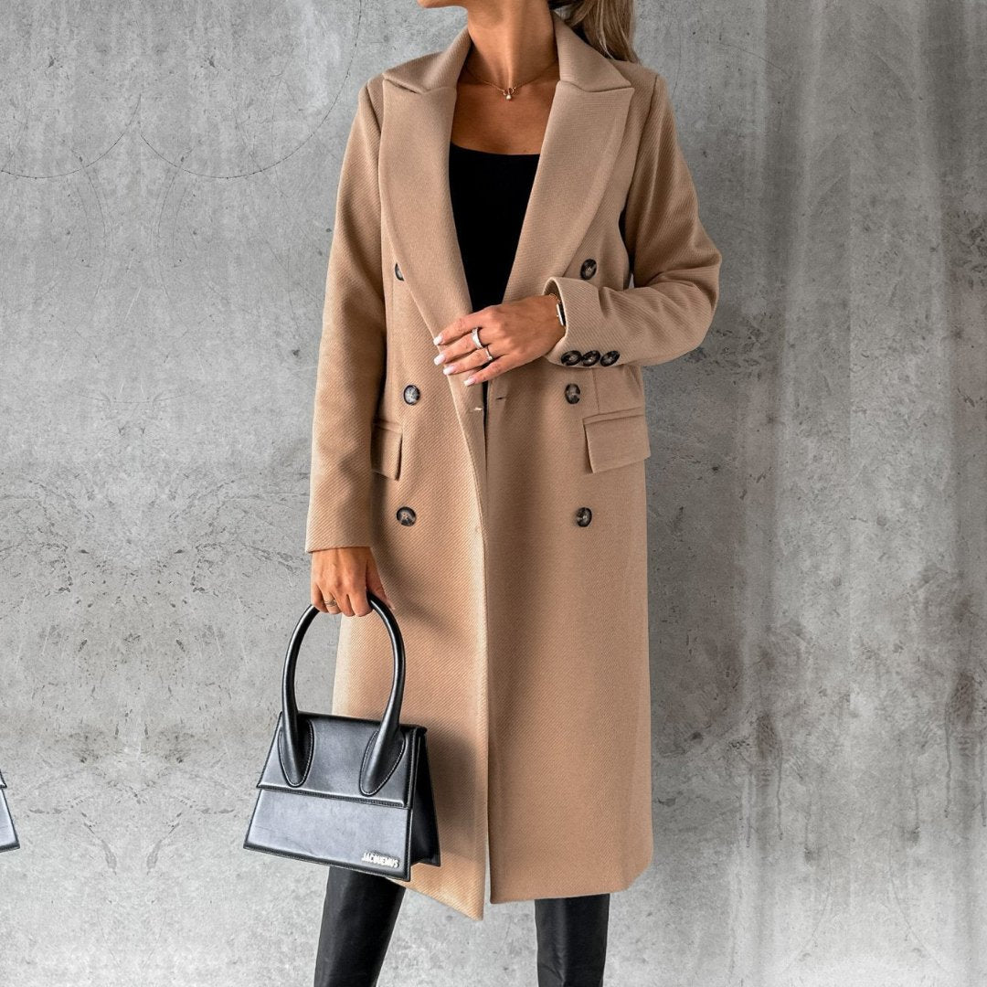 Ulara Winterjas - Een stijlvolle camel-kleurige lange winterjas voor dames, met een dubbele rij knopen, brede revers en praktische zakken. Perfect gecombineerd met een zwarte handtas en moderne outfit voor een elegante, functionele look.