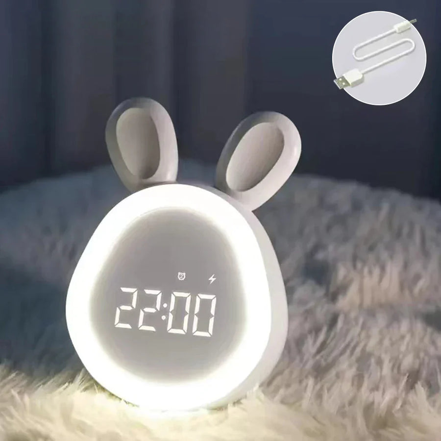 Urania alarmklok in de vorm van een konijn, met verlicht LED-display dat de tijd 22:00 aangeeft. De klok staat op een zachte ondergrond en heeft een schattig en functioneel ontwerp. In de hoek is een USB-oplaadkabel zichtbaar, wat aangeeft dat de klok eenvoudig oplaadbaar is. Perfect als nachtlampje en wekker.