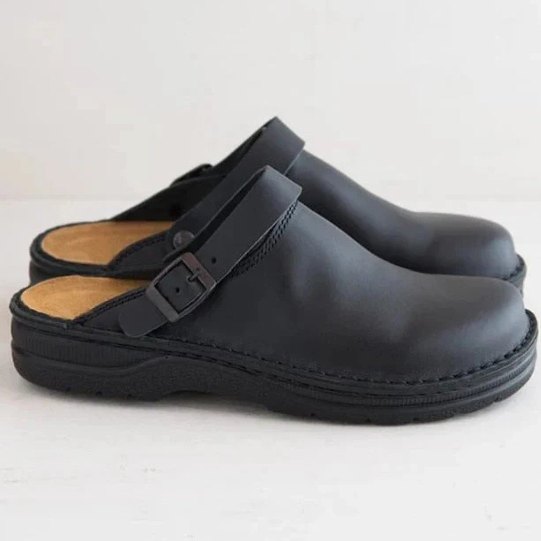 Afbeelding van de Urbano loafers in een klassiek zwart leren ontwerp. Deze comfortabele instappers hebben een open hiel en een verstelbare gesp voor een persoonlijke pasvorm. De stevige zool biedt uitstekende grip en ondersteuning, terwijl het zachte voetbed zorgt voor langdurig draagcomfort. Perfect voor zowel binnen- als buitengebruik, met een tijdloze en veelzijdige uitstraling.