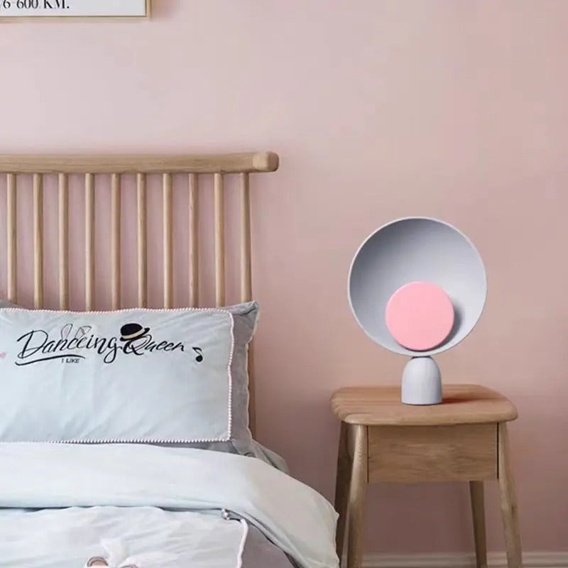 Wavello nachtlamp op een houten nachtkastje naast een bed, met een moderne en minimalistische uitstraling. De lamp heeft een witte, kegelvormige reflector en een zachte roze cirkel in het midden. Het sfeervolle licht voegt een kalmerende ambiance toe aan de slaapkamer. Perfect als decoratief accent voor een rustgevende en stijlvolle slaapomgeving.